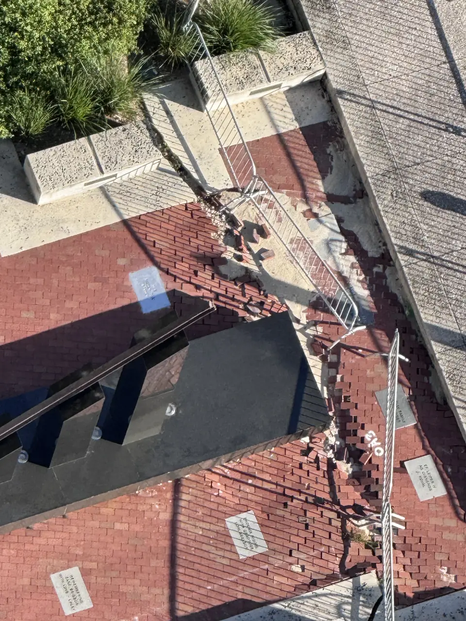 Overhead view of the Riverwalk 9/11 Monument, with displaced pavers and barricades along the edge of its base.