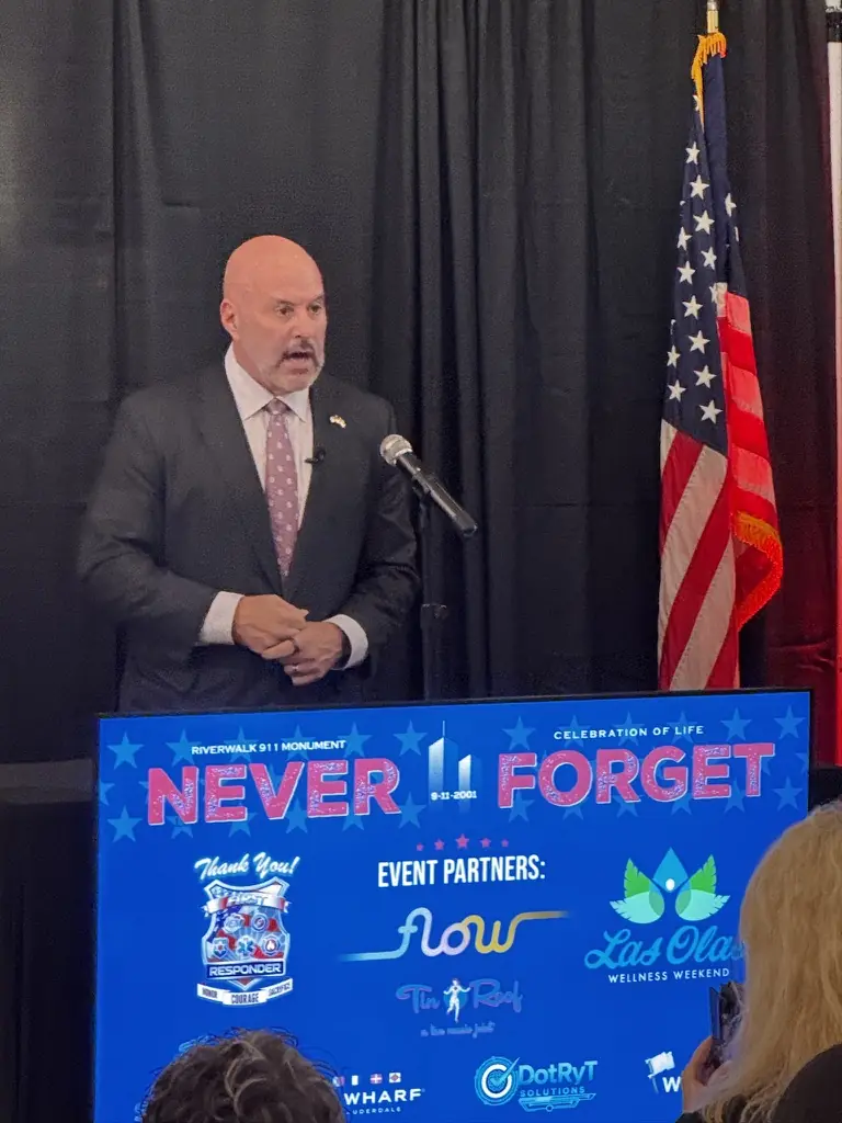 A speaker at the Never Forget podium beside the American flag.