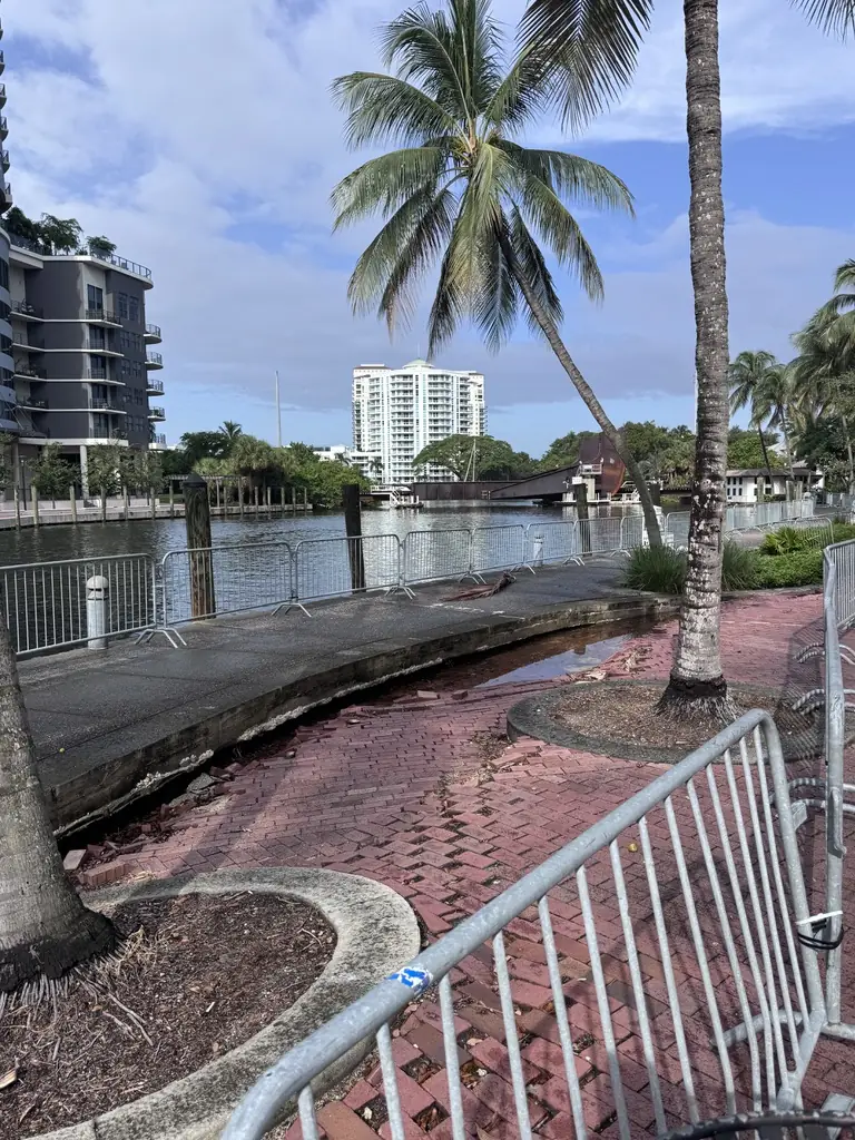 Damaged brick pavers behind the barricade at the river's edge.